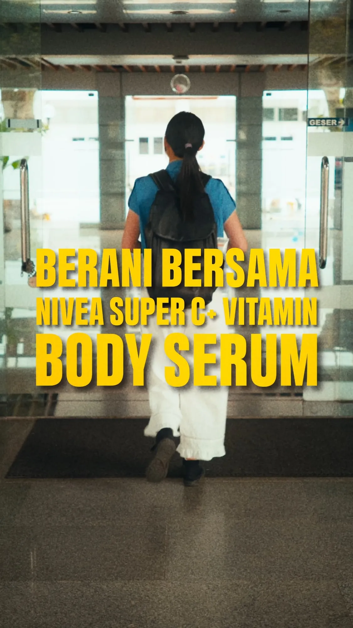 A still from the ad, a student with a backpack walking through glass doors under the words "Berani Bersama NIVEA Super C+ Vitamin Body Serum".
